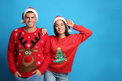 Photo of Couple in Christmas sweaters and Santa hats on blue background, space for text