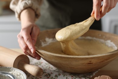 Photo of Woman kneading dough with spoon in bowl at wooden table indoors, closeup
