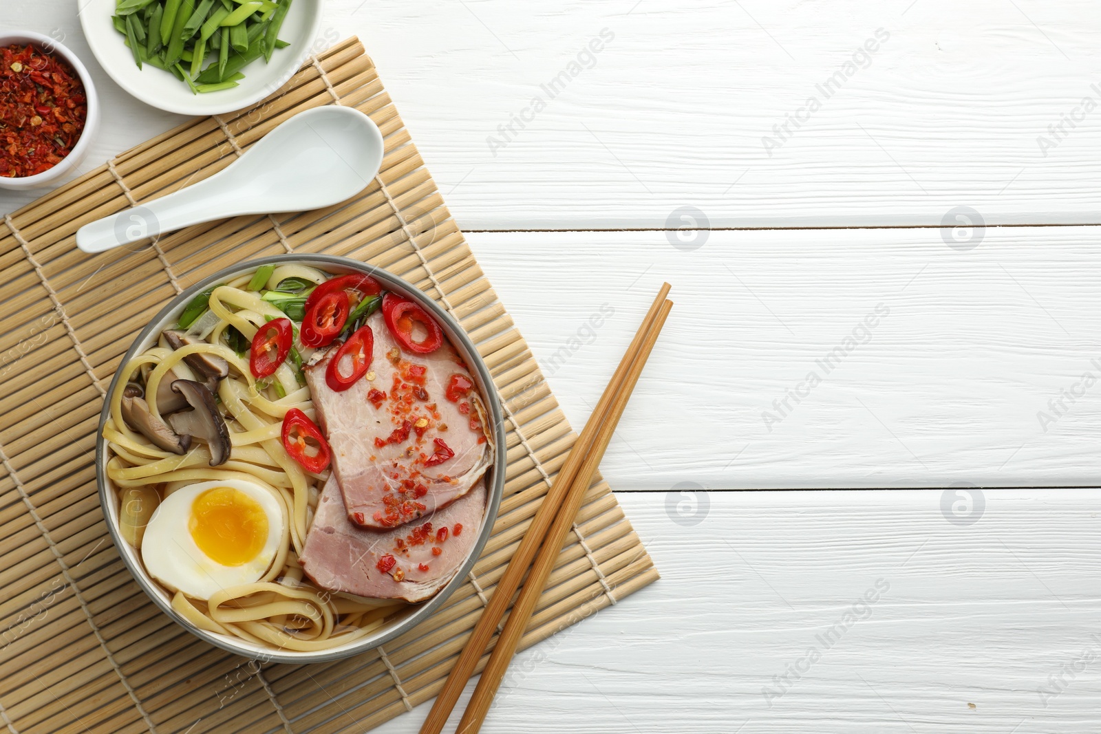 Photo of Delicious ramen in bowl served on white wooden table, flat lay and space for text. Noodle soup