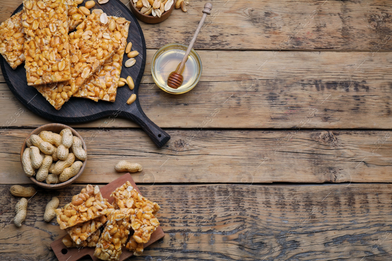 Photo of Delicious peanut kozinaki bars, nuts and honey on wooden table, flat lay. Space for text