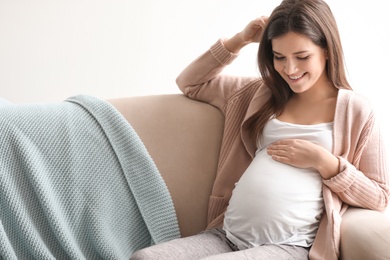 Photo of Young pregnant woman sitting on couch in living room