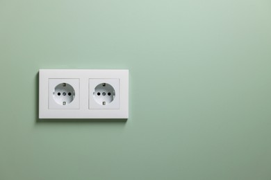 Photo of Electric power sockets on light green wall indoors, space for text