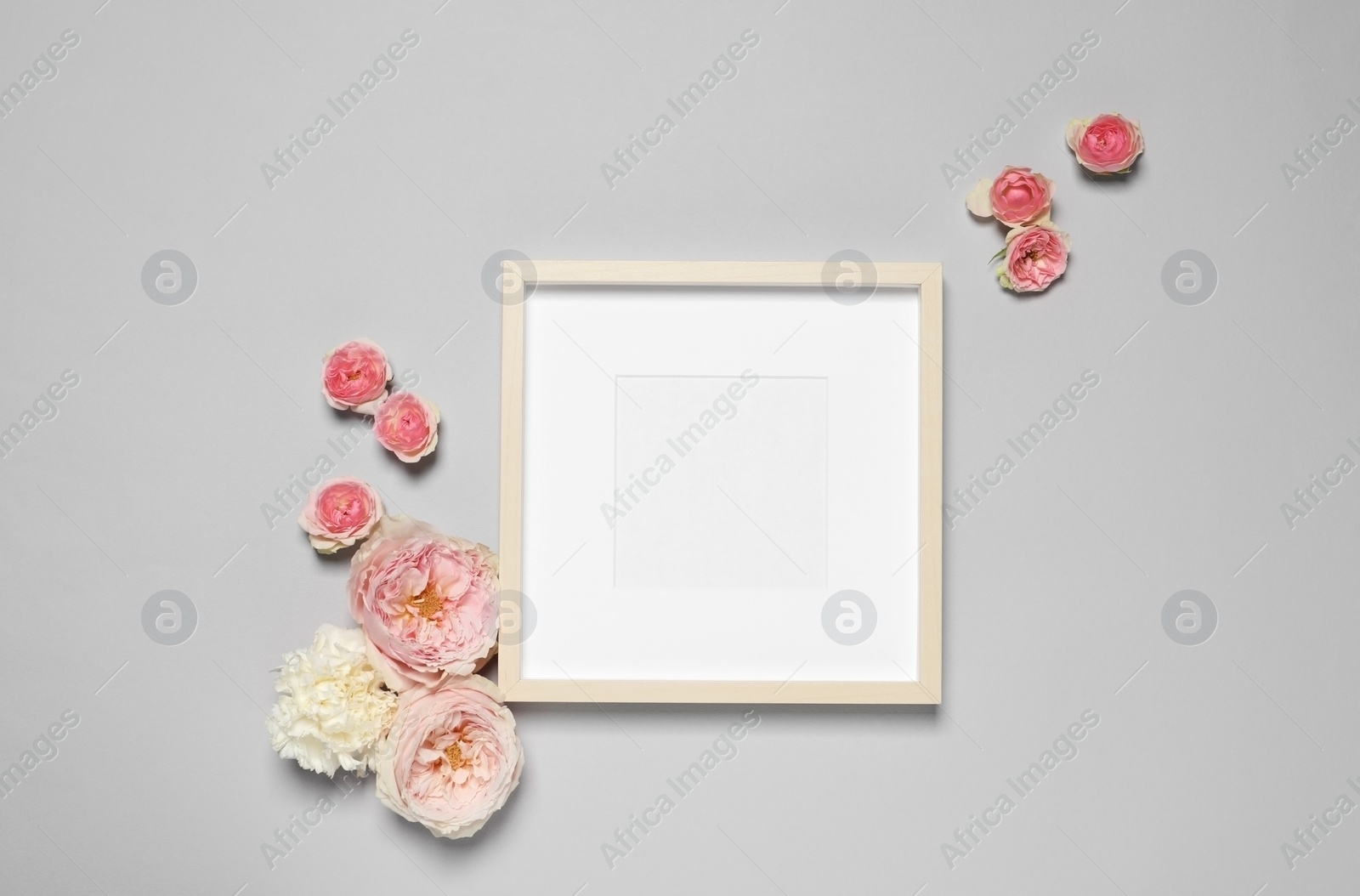 Photo of Empty photo frame and beautiful flowers on light gray background, flat lay. Space for design