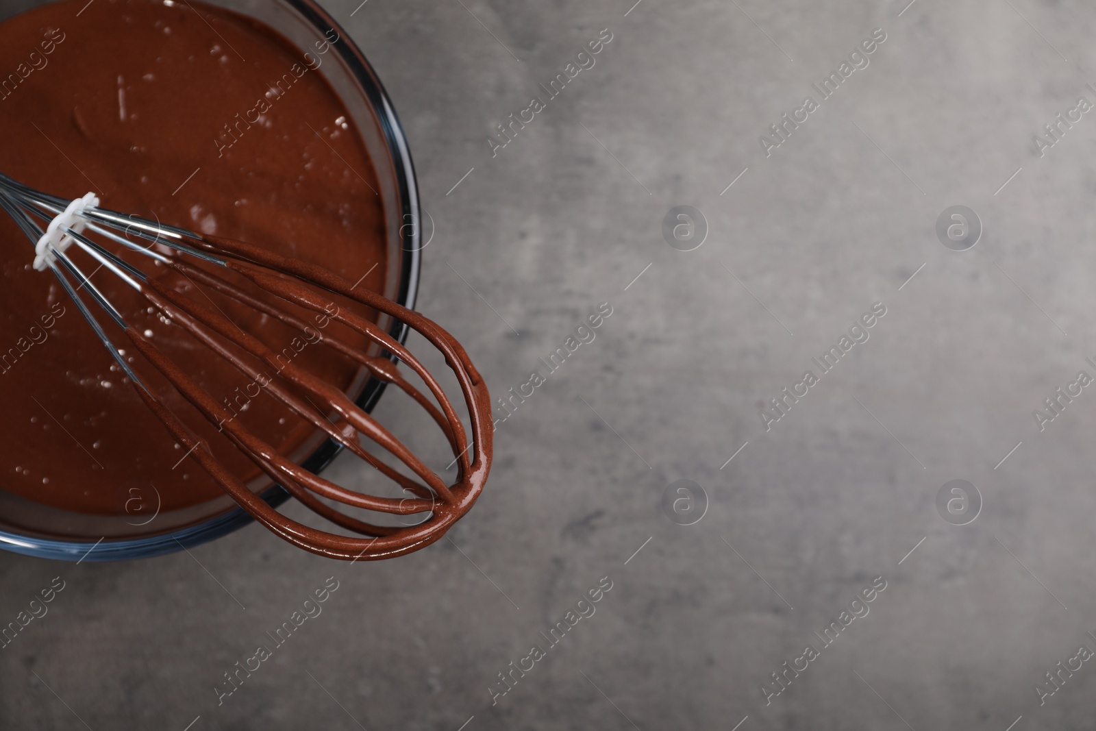 Photo of Bowl of chocolate cream and whisk on gray table, top view. Space for text