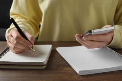 Woman with pen, notepads and smartphone at wooden table, closeup