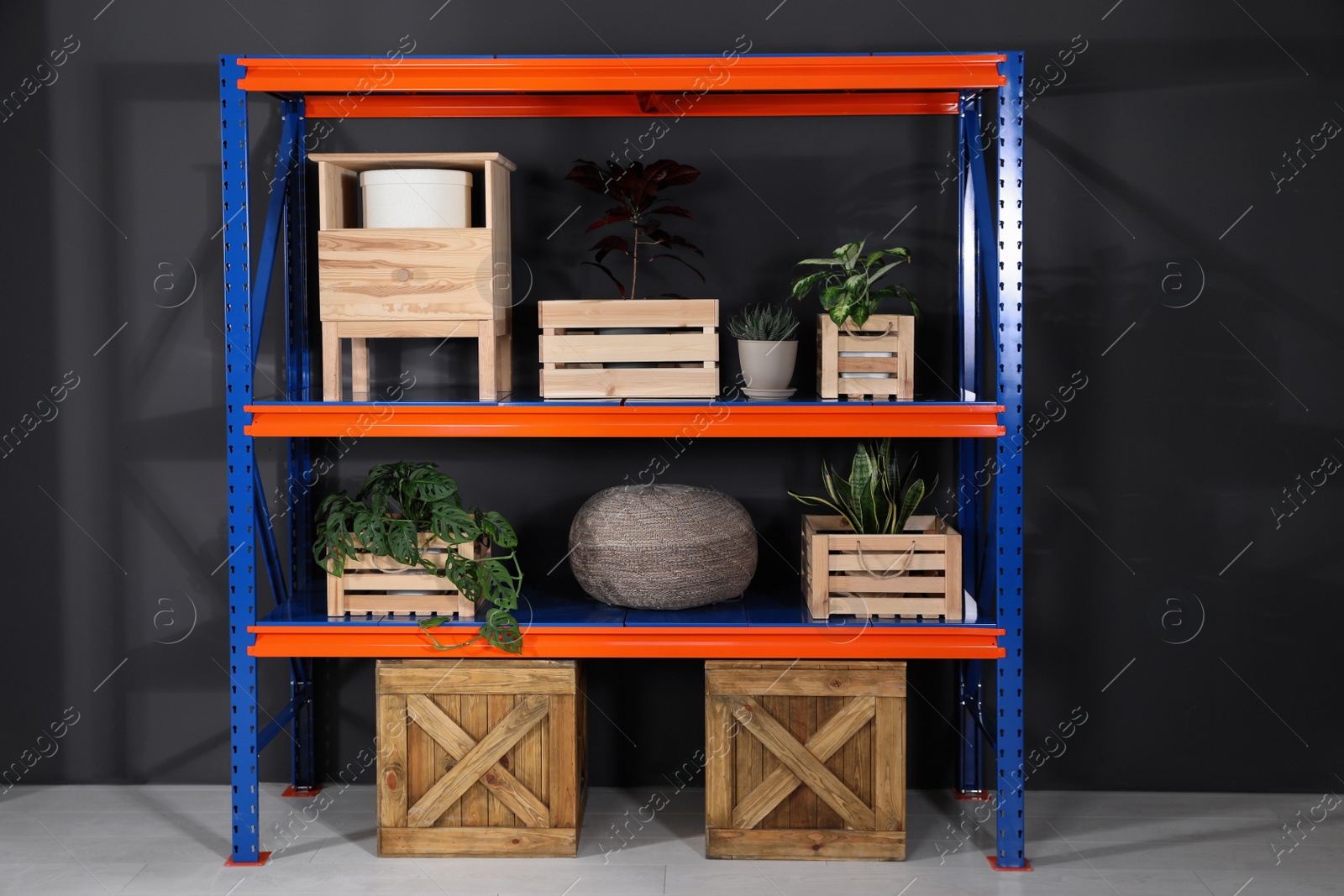 Photo of Metal shelving unit with wooden crates and different household stuff near black wall indoors