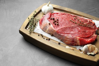 Photo of Wooden tray with piece of raw meat, garlic and thyme on grey table