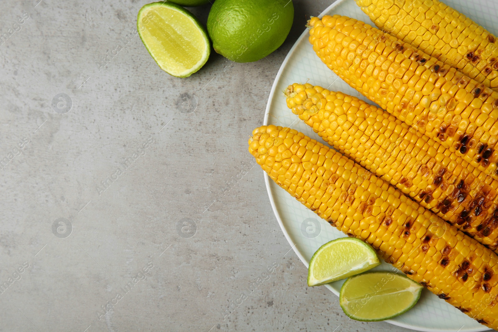 Photo of Plate of grilled corn cobs and limes on grey table, flat lay. Space for text