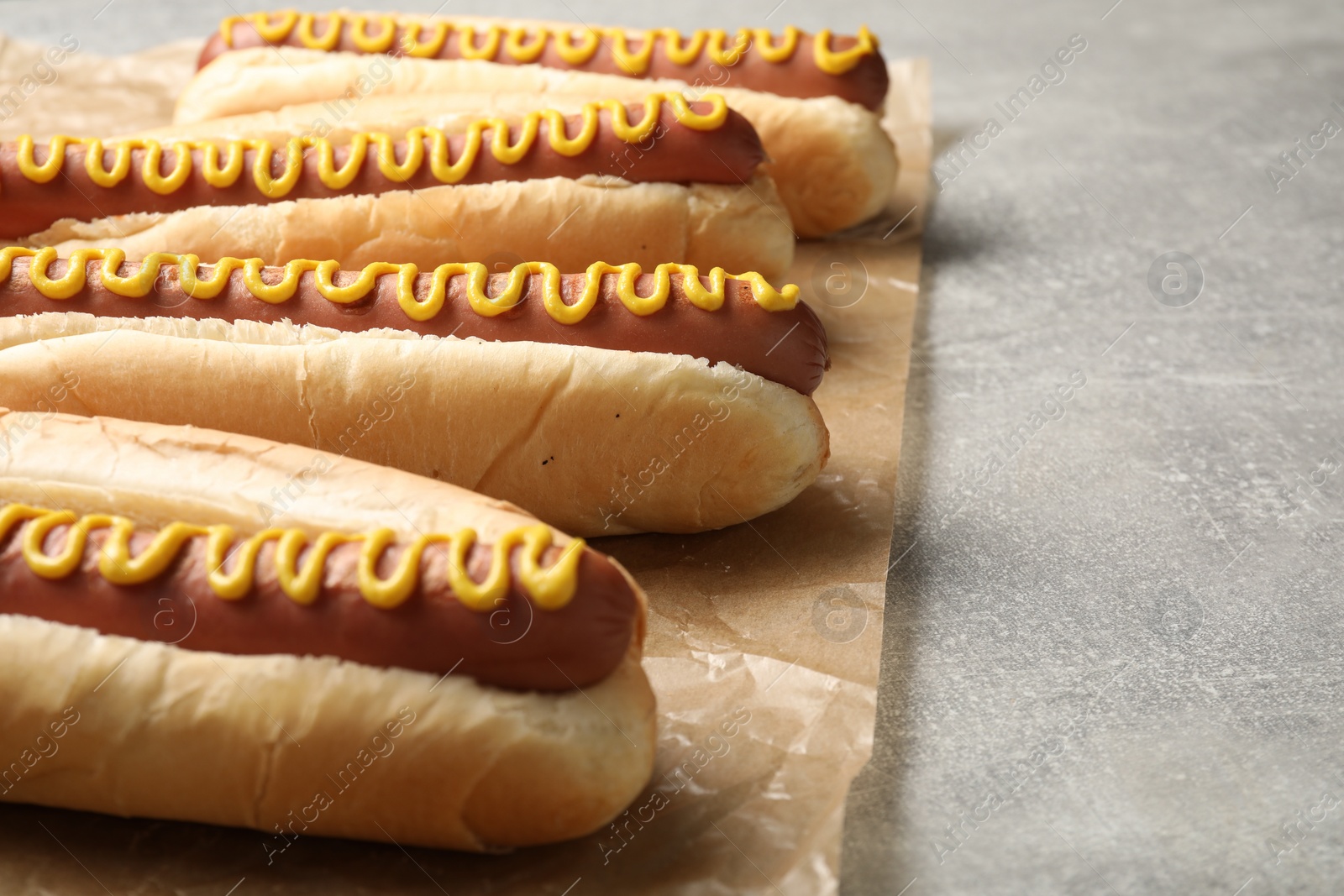 Photo of Fresh delicious hot dogs with mustard on light grey table, closeup. Space for text