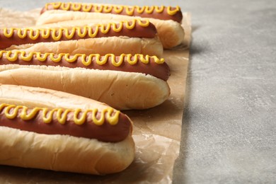 Fresh delicious hot dogs with mustard on light grey table, closeup. Space for text