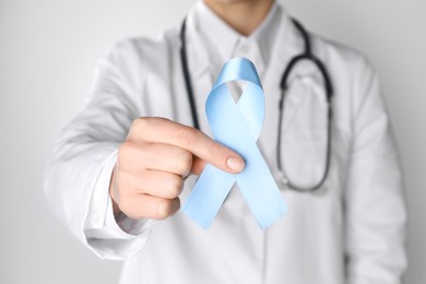 Photo of International Psoriasis Day. Doctor with light blue ribbon as symbol of support on white background, closeup