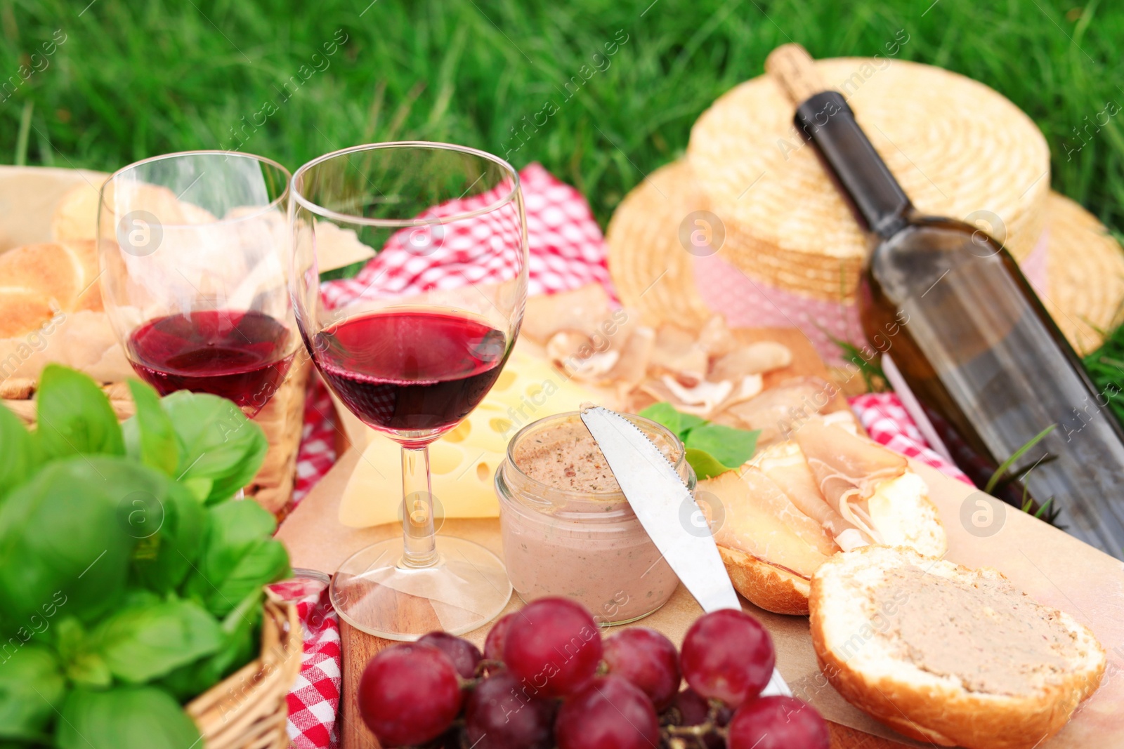 Photo of Closeup view of picnic blanket with wine and food on green grass