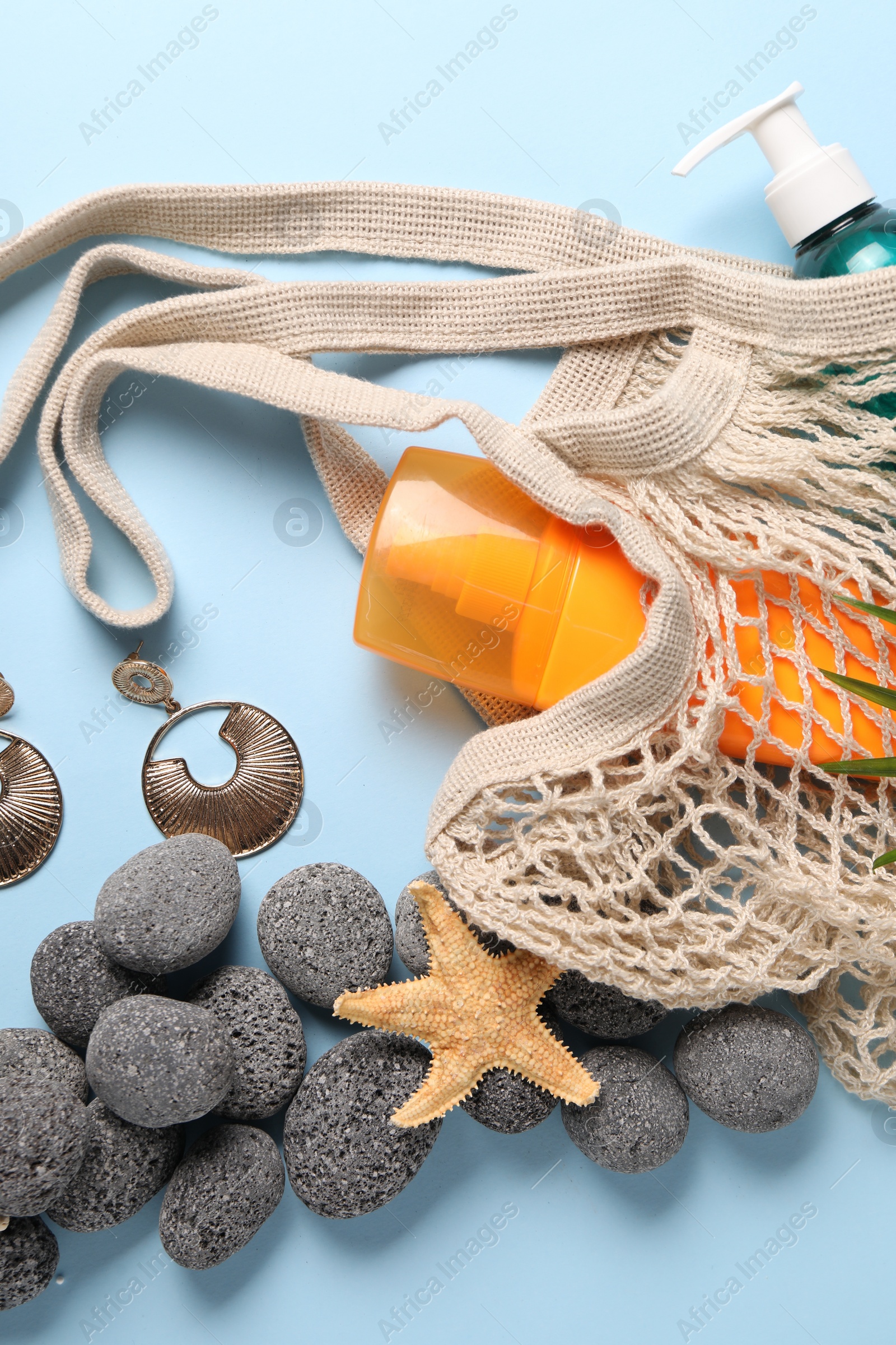 Photo of String bag and different beach accessories on light blue background, flat lay