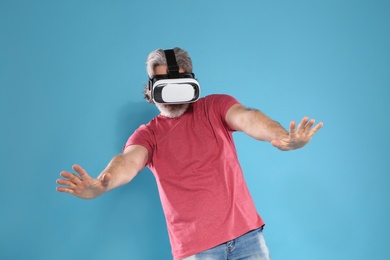 Emotional mature man playing video games with virtual reality headset on color background