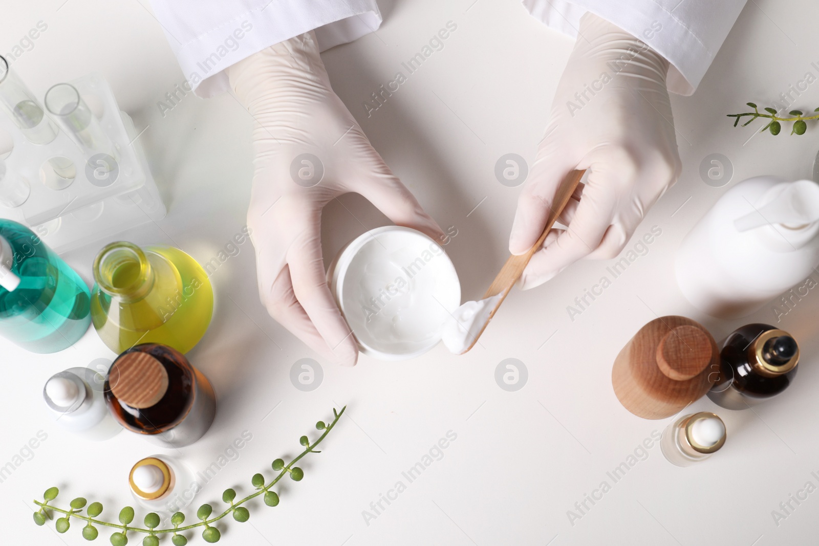 Photo of Dermatologist with jar testing cosmetic product at white table, top view