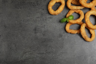 Photo of Fried onion rings and basil leaves on grey table, flat lay. Space for text