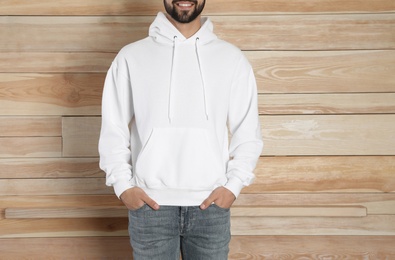 Photo of Young man in sweater at wooden wall, closeup. Mock up for design