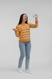 Smiling young woman taking selfie with smartphone on white background