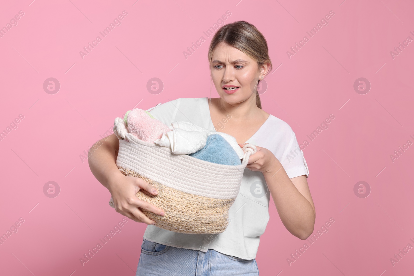 Photo of Young woman with basket full of laundry on pink background