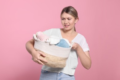 Photo of Young woman with basket full of laundry on pink background