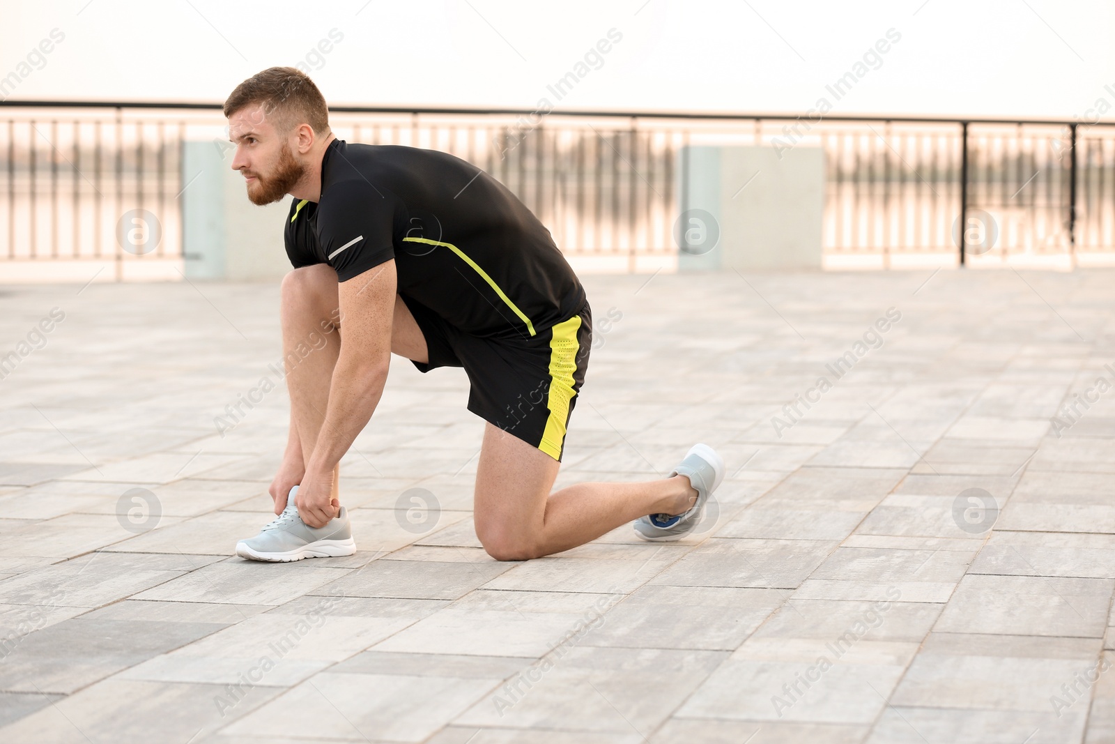 Photo of Young man tying shoelaces before running outdoors on sunny day