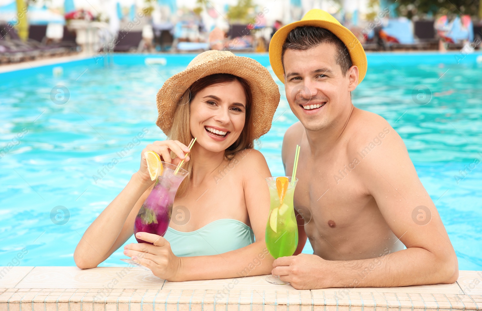 Photo of Happy couple with cocktails resting in blue swimming pool outdoors