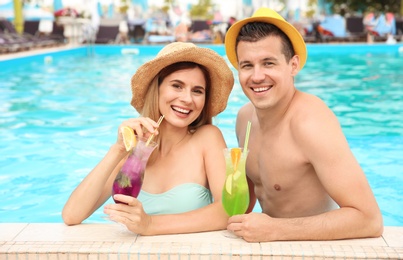 Happy couple with cocktails resting in blue swimming pool outdoors