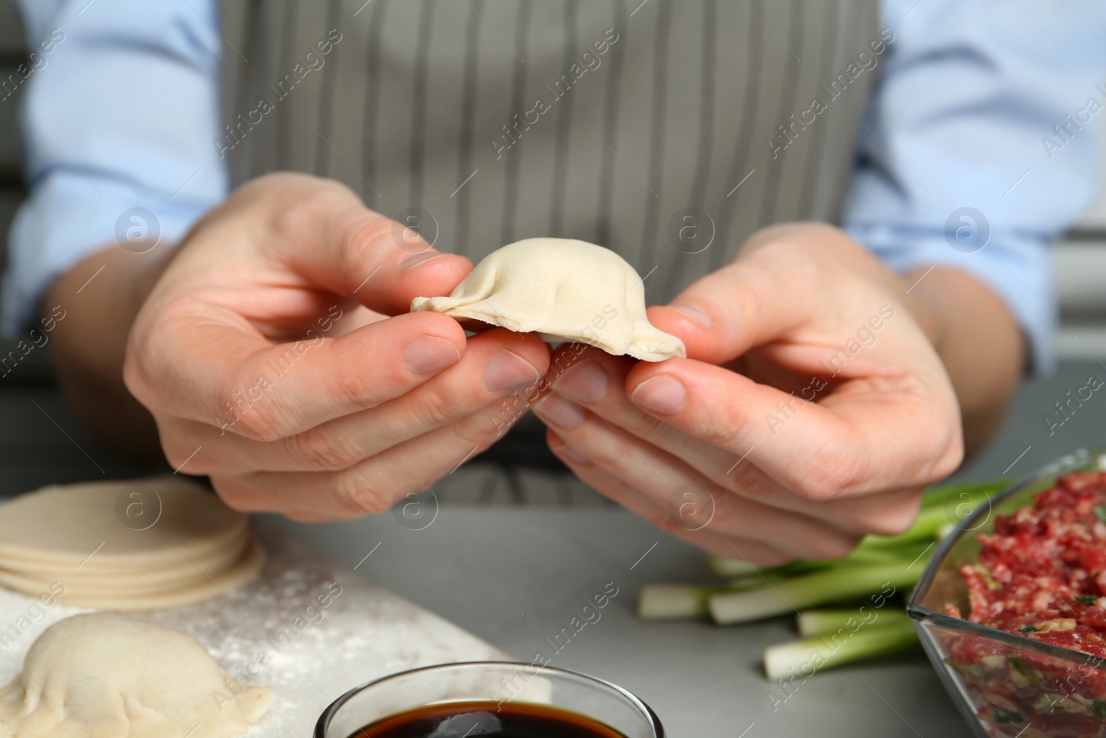 Photo of Woman making gyoza at light grey table, closeup