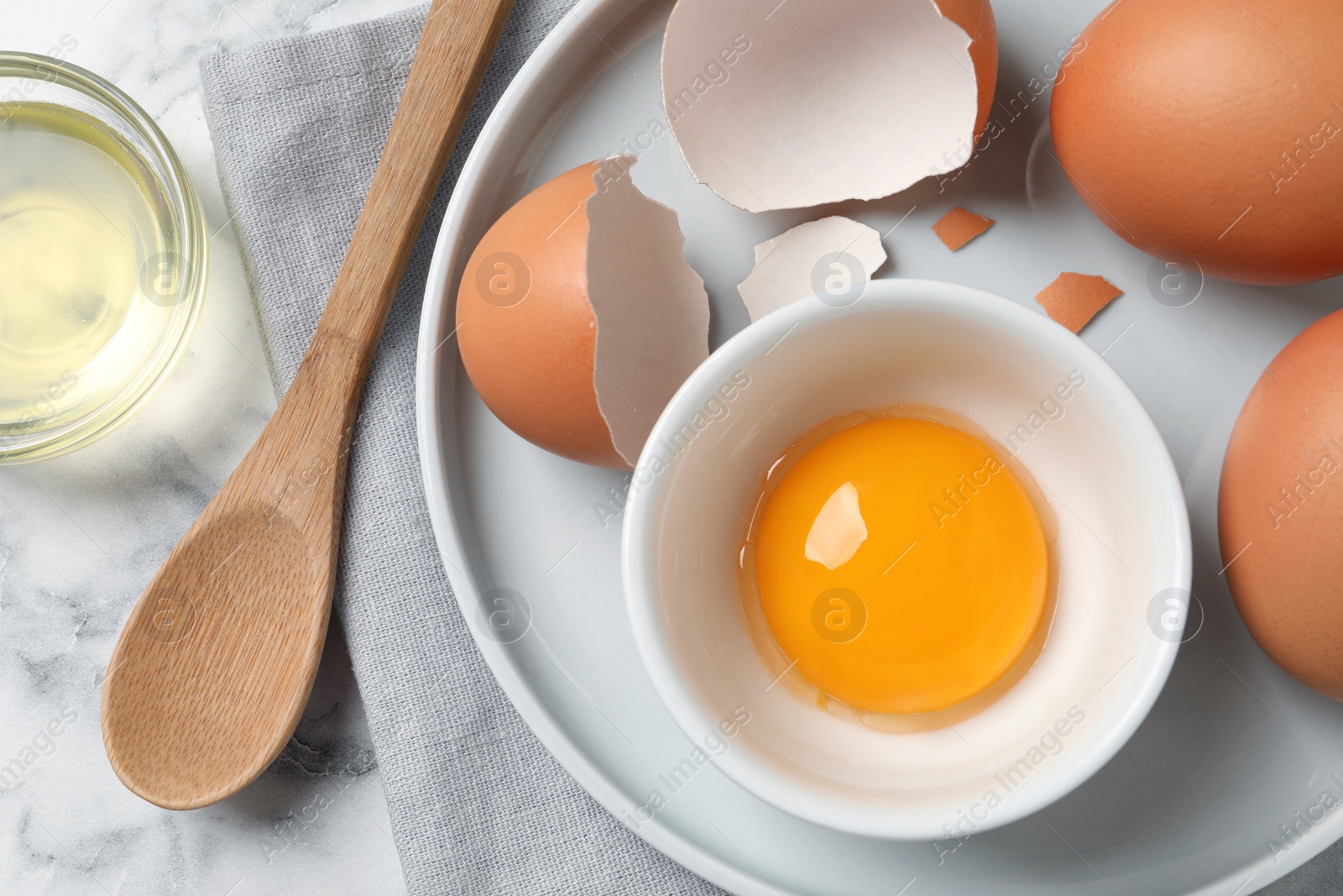 Photo of Chicken eggs and bowl with raw yolk on white marble table, flat lay