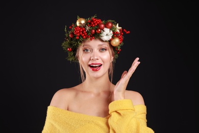 Beautiful young woman wearing Christmas wreath on black background