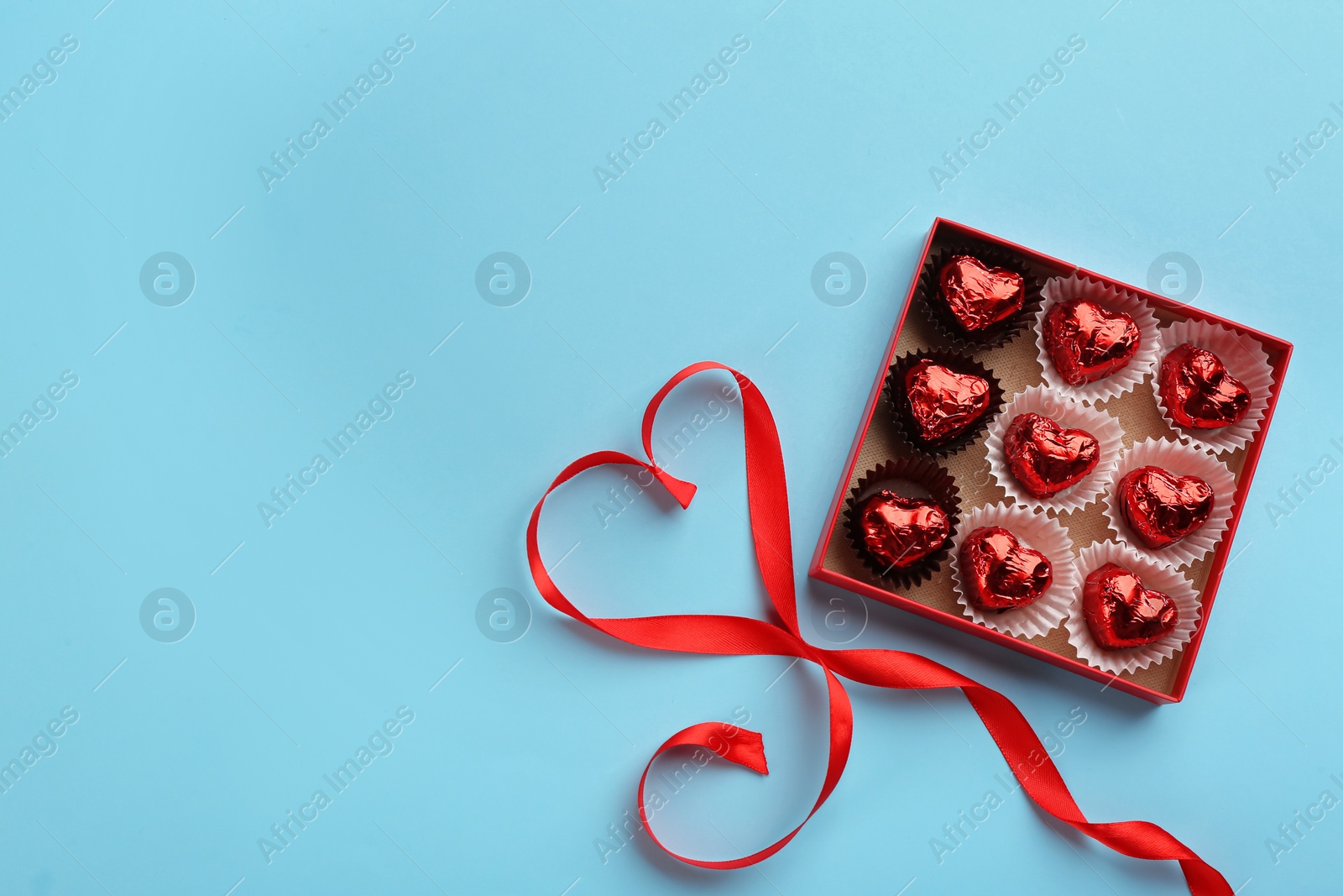 Photo of Heart shaped chocolate candies and ribbon on light blue background, flat lay. Space for text