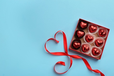 Heart shaped chocolate candies and ribbon on light blue background, flat lay. Space for text