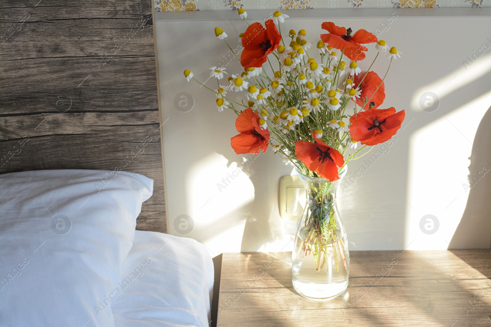 Photo of Glass vase with bouquet of beautiful wildflowers on nightstand in bedroom