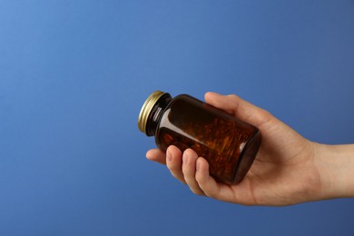 Photo of Woman holding jar with vitamin capsules on blue background, closeup