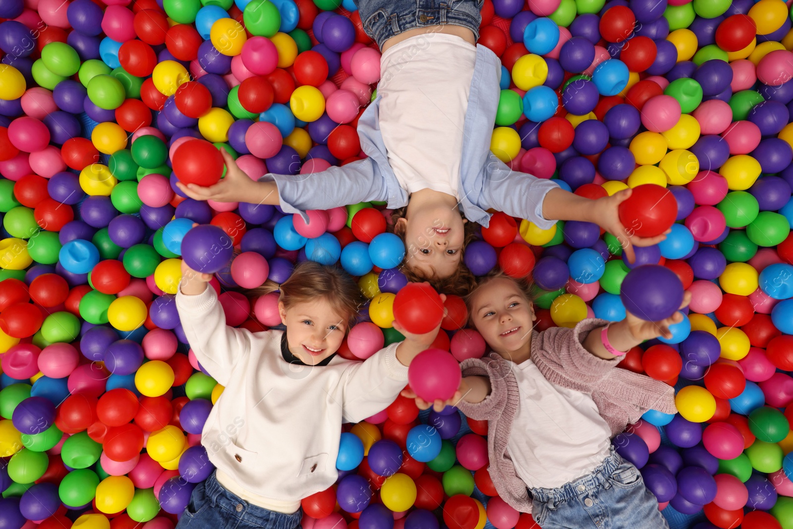 Photo of Happy little kids lying on many colorful balls, top view