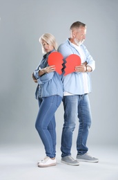 Photo of Mature couple with torn paper heart on grey background. Relationship problems