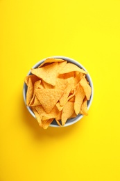 Tasty mexican nachos chips in bowl on yellow background, top view