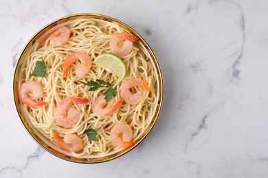 Tasty spaghetti with shrimps, lime and parsley in bowl on white marble table, top view. Space for text