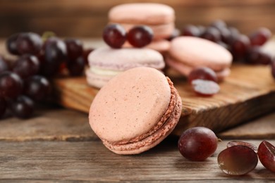 Photo of Delicious macarons and grapes on wooden table, closeup