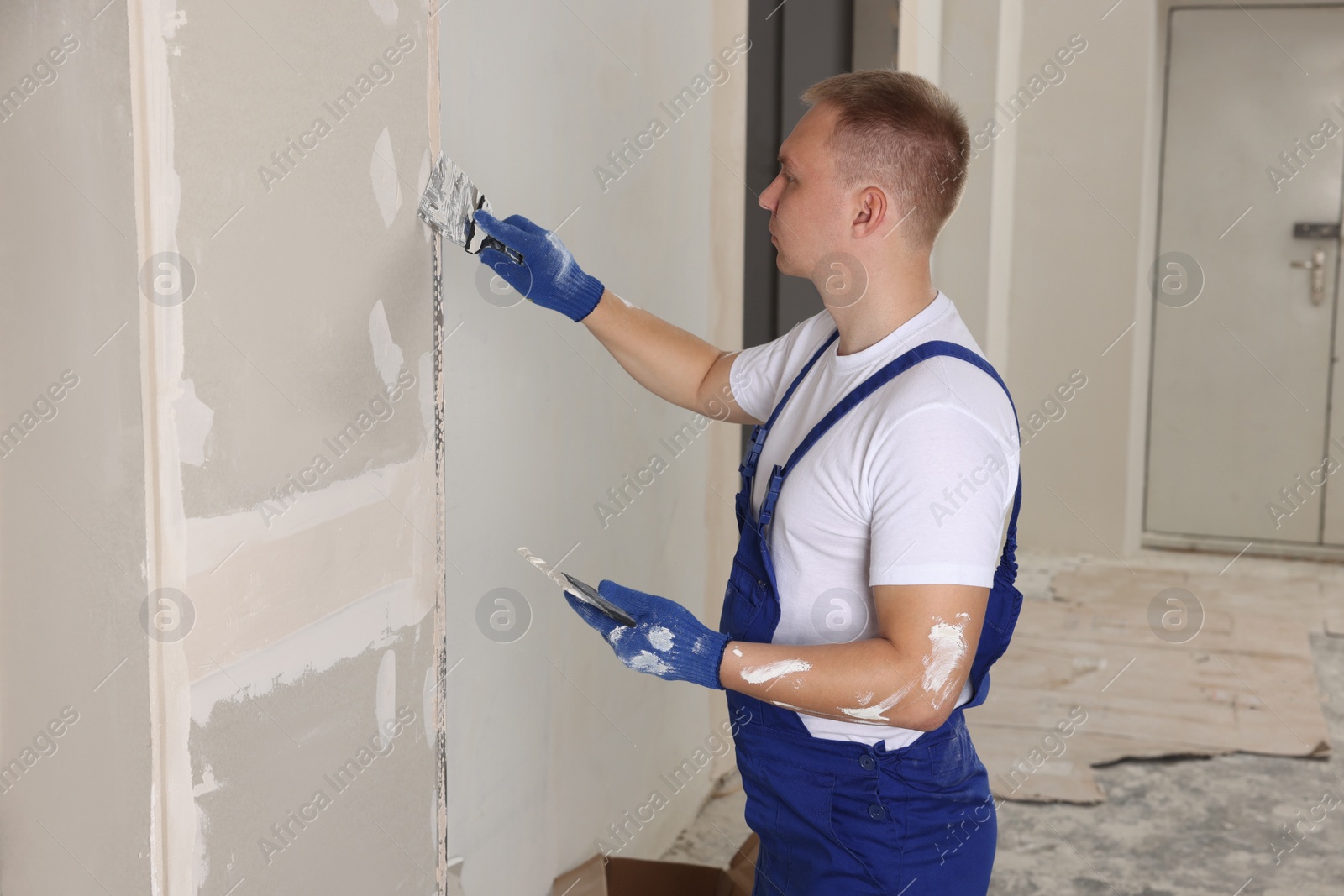 Photo of Man plastering wall with putty knife indoors. Home renovation