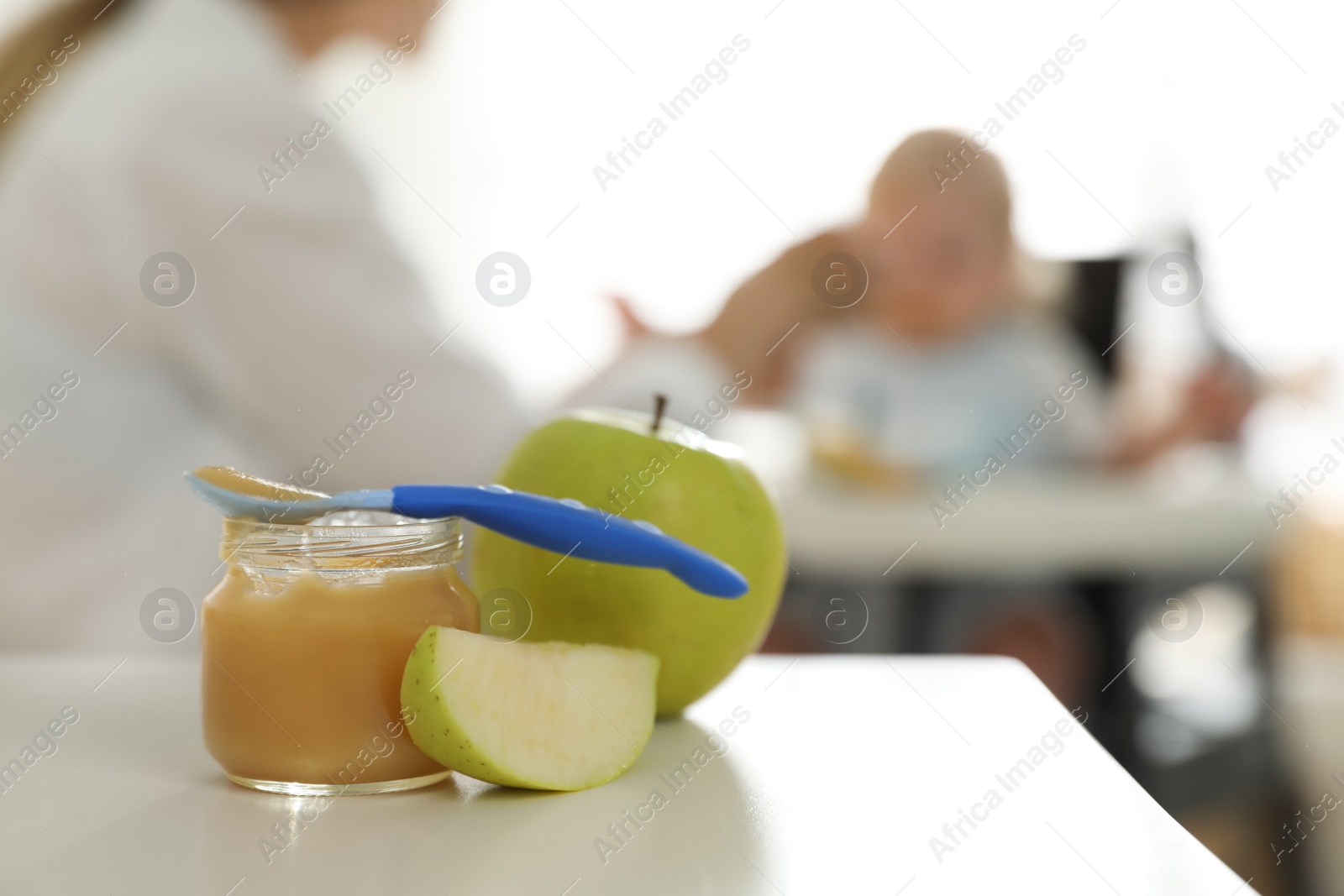 Photo of Mother feeding her little baby at home, focus on healthy fruit puree and fresh apples