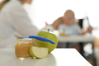 Mother feeding her little baby at home, focus on healthy fruit puree and fresh apples