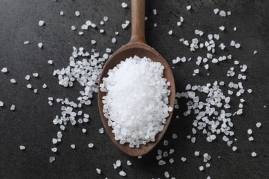 Natural salt and wooden spoon on black table, top view