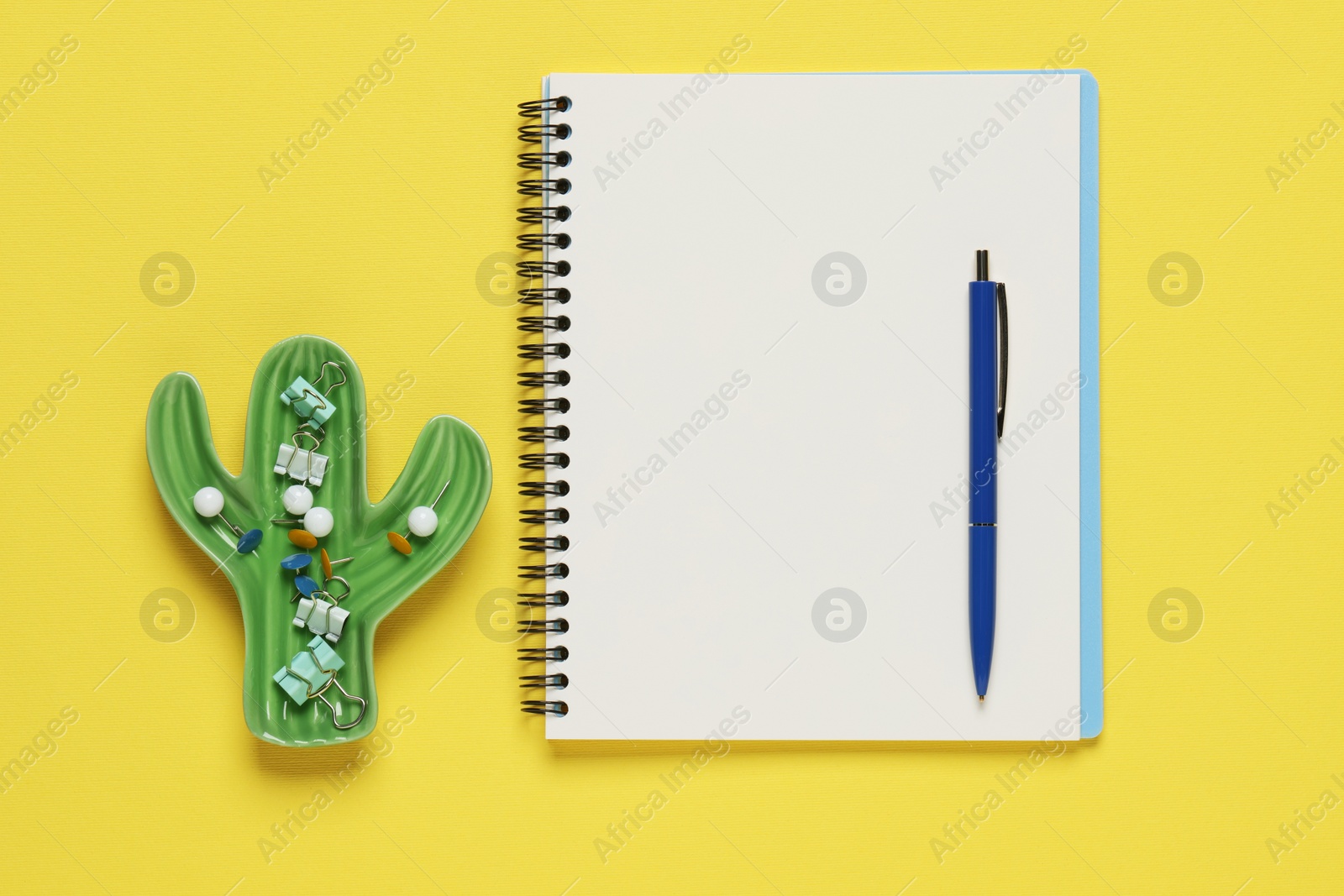 Photo of Ballpoint pen, notebook and different clips on yellow background, flat lay