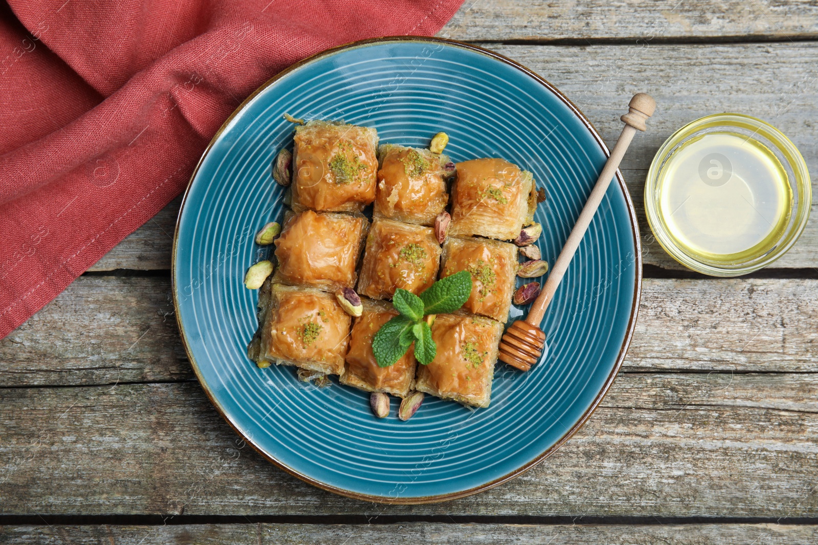 Photo of Delicious baklava with pistachios, honey and mint on wooden table, flat lay