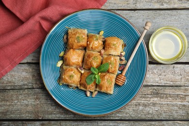 Photo of Delicious baklava with pistachios, honey and mint on wooden table, flat lay