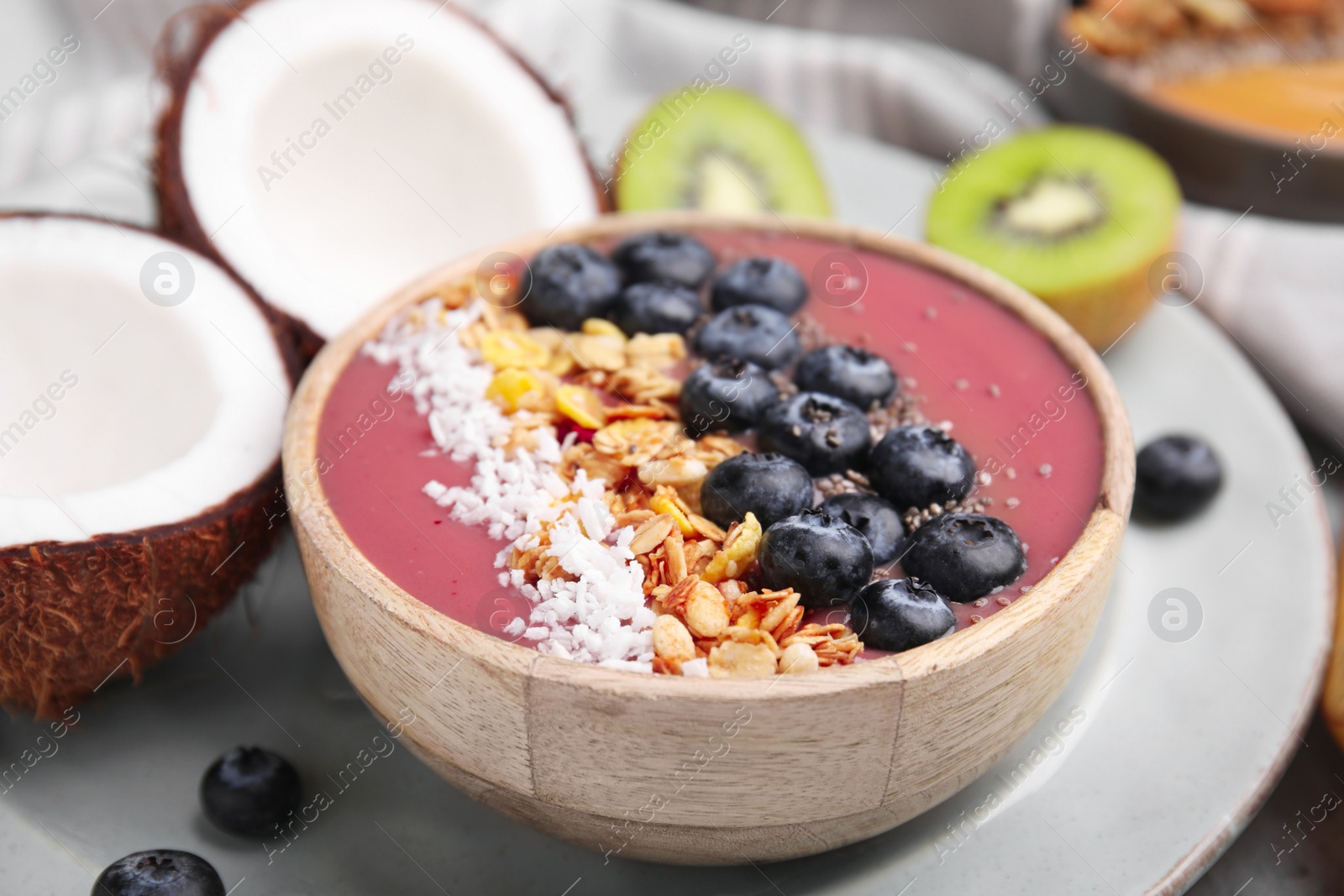 Photo of Bowl of delicious fruit smoothie with fresh blueberries, granola and coconut flakes on tray, closeup