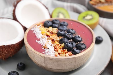 Bowl of delicious fruit smoothie with fresh blueberries, granola and coconut flakes on tray, closeup