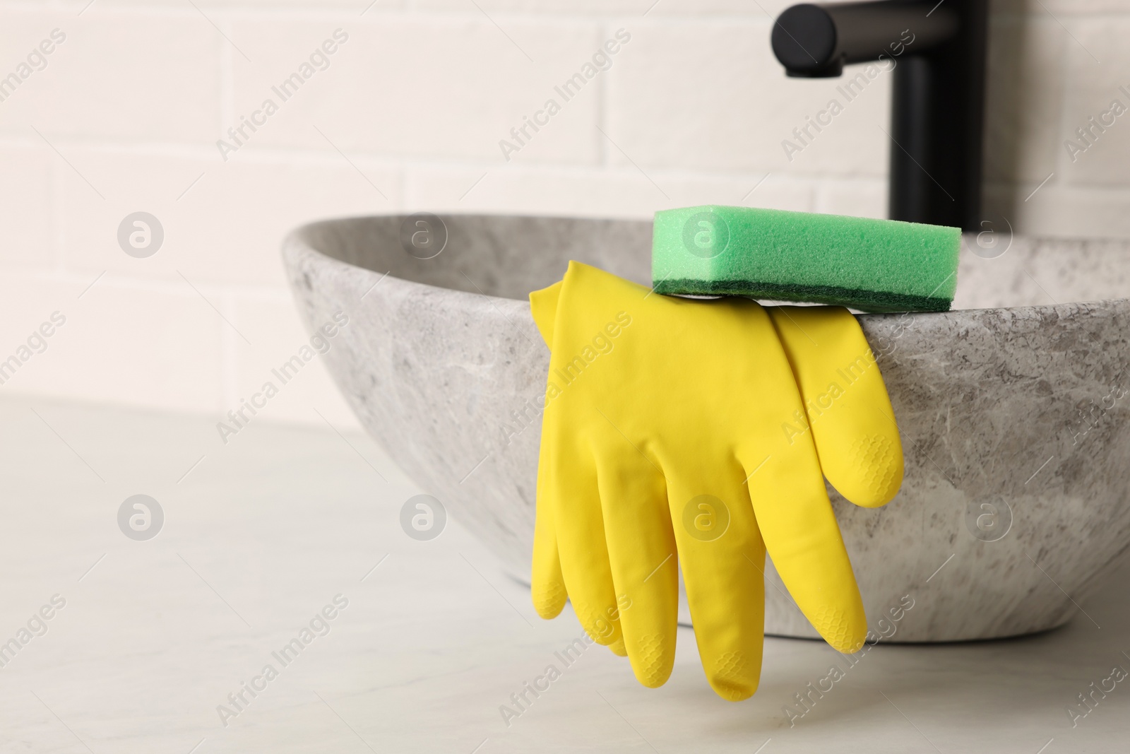 Photo of Sponge and rubber gloves on bathroom sink indoors. Space for text