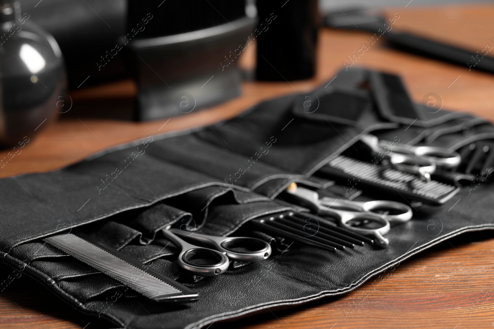 Photo of Hairdresser tools. Professional scissors and combs in leather organizer on wooden table, closeup